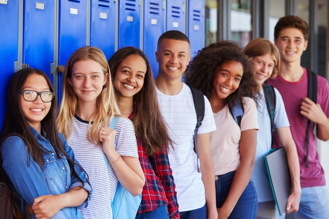 Smiling adolescent students with backpacks standing in front of their lockers at school
